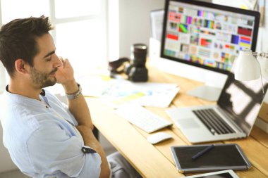 İnternette çalışırken bilgisayarın ve dizüstü bilgisayarın önünde grafik stüdyosunda oturan genç tasarımcının portresi