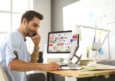 İnternette çalışırken bilgisayarın ve dizüstü bilgisayarın önünde grafik stüdyosunda oturan genç tasarımcının portresi