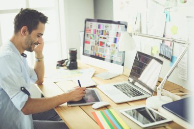 İnternette çalışırken bilgisayarın ve dizüstü bilgisayarın önünde grafik stüdyosunda oturan genç tasarımcının portresi