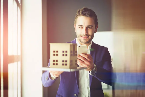 Affärsman som håller huset miniatyr på handen stående i office — Stockfoto