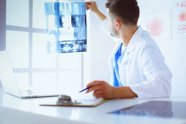 Fiatal orvos ül az irodájában, és elemzi a röntgen — Stock Fotó