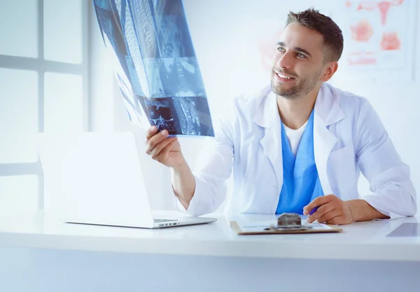 Молодий лікар сидить за своїм офісним столом і аналізує рентген — стокове фото