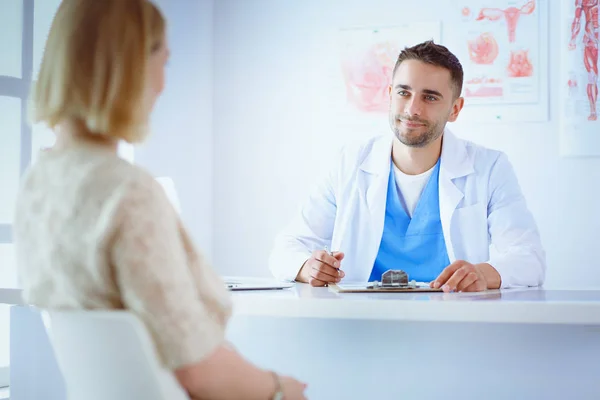 Snygg läkare pratar med ung kvinnlig patient och antecknar när han sitter på sitt kontor — Stockfoto
