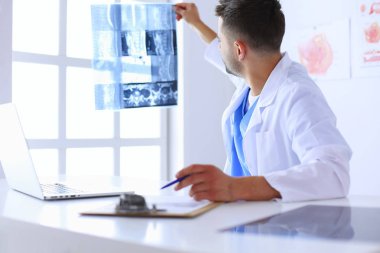 Genç doktor ofisinde oturuyor ve röntgen sonuçlarını inceliyor.