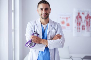 Genç ve kendinden emin erkek doktor portresi tıp ofisinde duruyor.