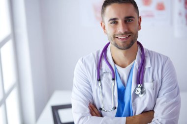Genç ve kendinden emin erkek doktor portresi tıp ofisinde duruyor.