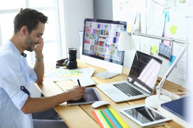 İnternette çalışırken bilgisayarın ve dizüstü bilgisayarın önünde grafik stüdyosunda oturan genç tasarımcının portresi