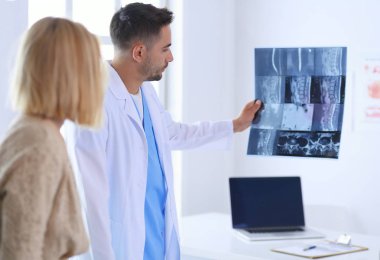 Yakışıklı doktor genç bayan hastasıyla konuşuyor ve ofisinde otururken notlar alıyor.