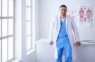 Genç ve kendinden emin erkek doktor portresi tıp ofisinde duruyor.