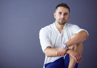 Gri arka planda yalnız oturan genç iş adamı