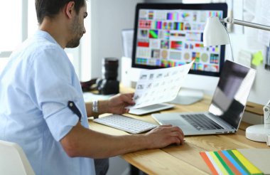 İnternette çalışırken bilgisayarın ve dizüstü bilgisayarın önünde grafik stüdyosunda oturan genç tasarımcının portresi