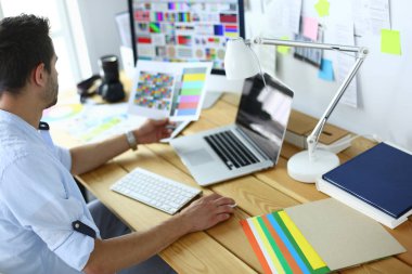 İnternette çalışırken bilgisayarın ve dizüstü bilgisayarın önünde grafik stüdyosunda oturan genç tasarımcının portresi