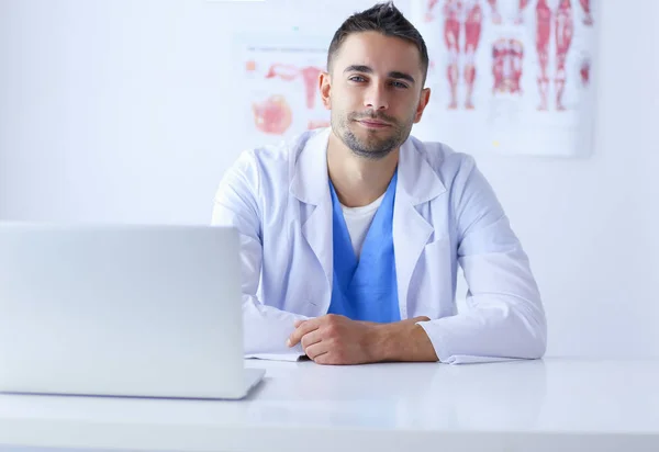 Retrato de um médico do sexo masculino com laptop sentado na mesa no consultório médico — Fotografia de Stock