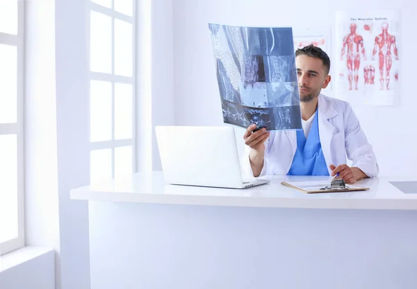 Молодой доктор сидит за своим столом и анализирует рентген — стоковое фото