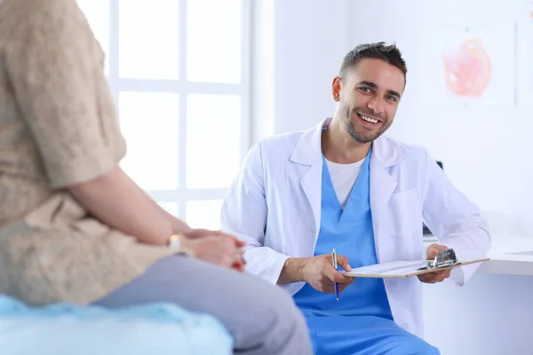 Schöner Arzt spricht mit junger Patientin und macht sich Notizen, während er in seinem Büro sitzt — Stockfoto