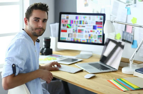 Portret młodego projektanta siedzącego w pracowni graficznej przed laptopem i komputerem podczas pracy online — Zdjęcie stockowe