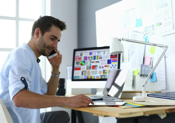 Портрет молодого дизайнера, сидящего в графической студии перед ноутбуком и компьютером во время работы в сети — стоковое фото