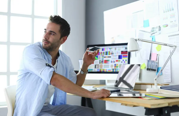 Πορτρέτο του νεαρού σχεδιαστή που κάθεται στο γραφιστικό στούντιο μπροστά από το laptop και τον υπολογιστή ενώ εργάζεται στο διαδίκτυο — Φωτογραφία Αρχείου