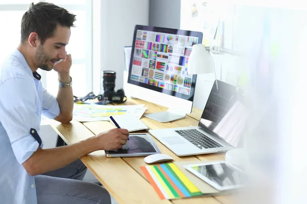 Portretul unui tânăr designer care stă la un studio grafic în fața laptopului și computerului în timp ce lucrează online — Fotografie, imagine de stoc