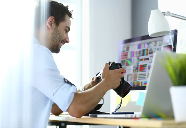 Retrato del joven diseñador sentado en el estudio gráfico frente a la computadora portátil y el ordenador mientras trabaja en línea — Foto de Stock