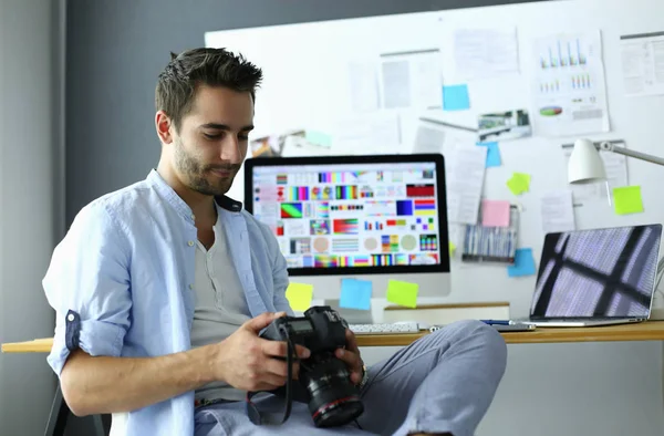 Retrato del joven diseñador sentado en el estudio gráfico frente a la computadora portátil y el ordenador mientras trabaja en línea — Foto de Stock