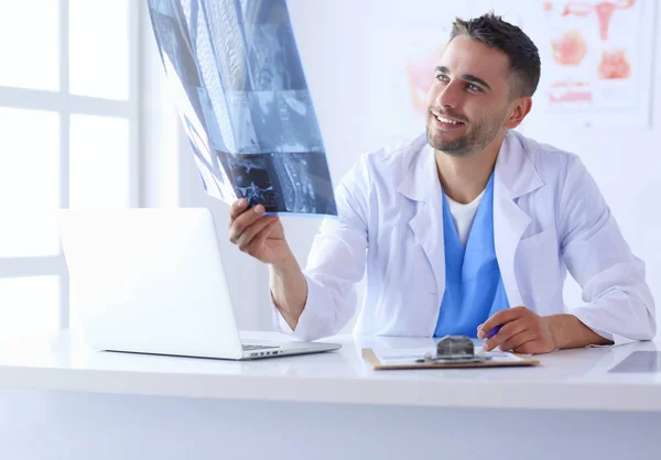 Junger Arzt sitzt an seinem Schreibtisch und analysiert ein Röntgenbild — Stockfoto