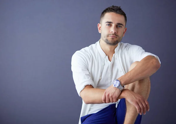 Young businessman sitting isolated on grey background — Stock Photo, Image