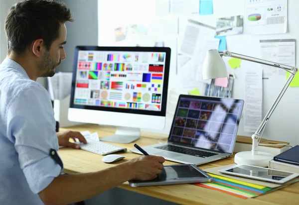 Retrato de jovem designer sentado no estúdio gráfico na frente de laptop e computador enquanto trabalhava online — Fotografia de Stock