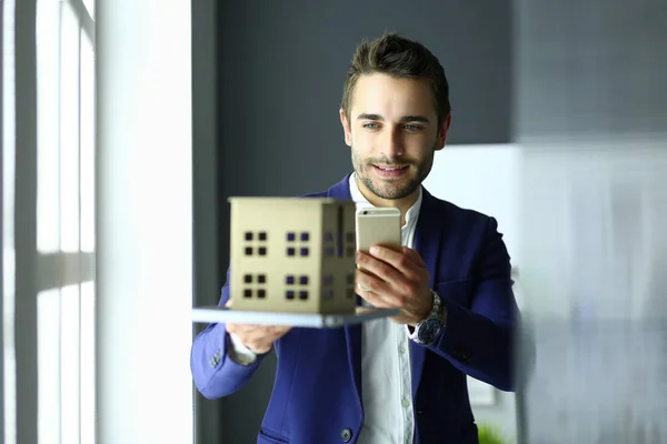 Homme d'affaires tenant maison miniature à portée de main debout dans le bureau — Photo