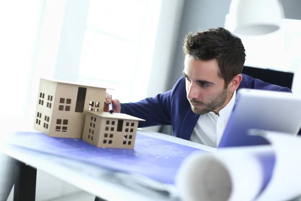Podnikatel, drží miniaturní dům na ruce postavení v úřadu — Stock fotografie