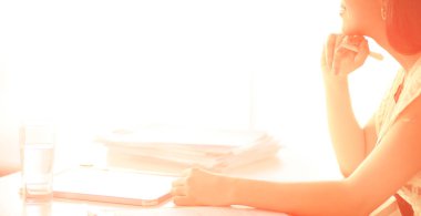 Elinde evrakları olan kadın masanın üstünde oturuyor.