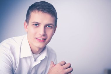 Gri arka plan üzerinde oturan gülümseyen genç adam portresi. Genç adam portresi