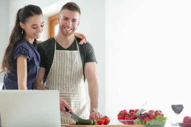 Sebze doğrayan genç bir adam ve mutfakta dizüstü bilgisayarı olan bir kadın.