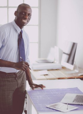 Ofiste bilgisayar ve planlarla çalışan Afrikalı Amerikalı bir mimar.