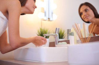 Genç bir kadın banyoda yüzünü temiz suyla yıkıyor.