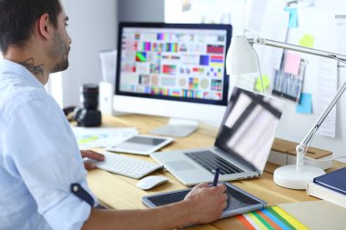 İnternette çalışırken bilgisayarın ve dizüstü bilgisayarın önünde grafik stüdyosunda oturan genç tasarımcının portresi.