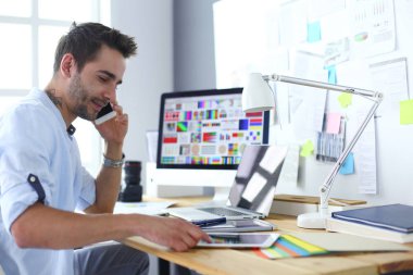 İnternette çalışırken bilgisayarın ve dizüstü bilgisayarın önünde grafik stüdyosunda oturan genç tasarımcının portresi.