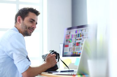 İnternette çalışırken bilgisayarın ve dizüstü bilgisayarın önünde grafik stüdyosunda oturan genç tasarımcının portresi.