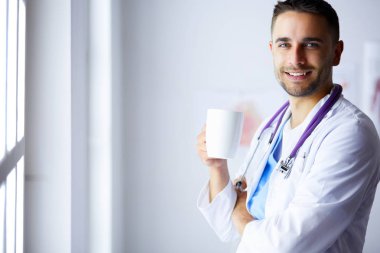 Elinde kahve fincanı olan genç bir doktor.