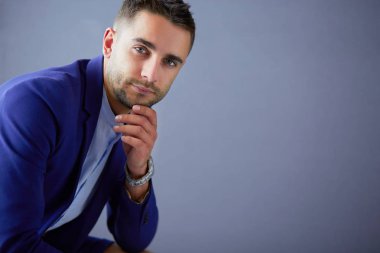 Gri arka planda yalnız oturan genç iş adamı