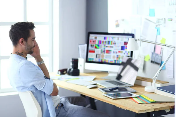 Porträt eines jungen Designers, der im Grafikstudio vor Laptop und Computer sitzt, während er online arbeitet. — Stockfoto