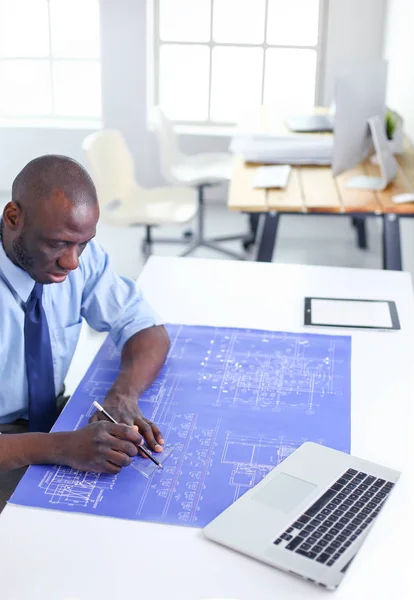 Afrikansk amerikansk arkitekt arbejder med computer og tegninger på kontoret - Stock-foto