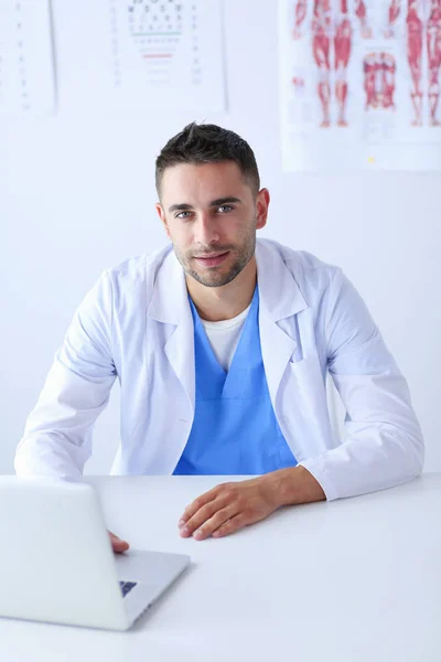 Portrét mužského lékaře s laptopem, který sedí za stolem v lékařské ordinaci — Stock fotografie