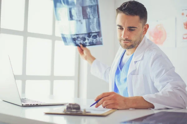 Молодий лікар сидить за своїм офісним столом і аналізує рентген — стокове фото