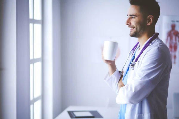 Joven médico con taza de café en el consultorio médico — Foto de Stock