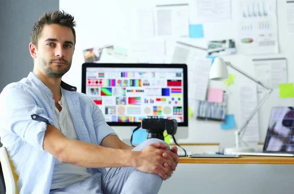 Retrato del joven diseñador sentado en el estudio gráfico frente a la computadora portátil y el ordenador mientras trabaja en línea. — Foto de Stock