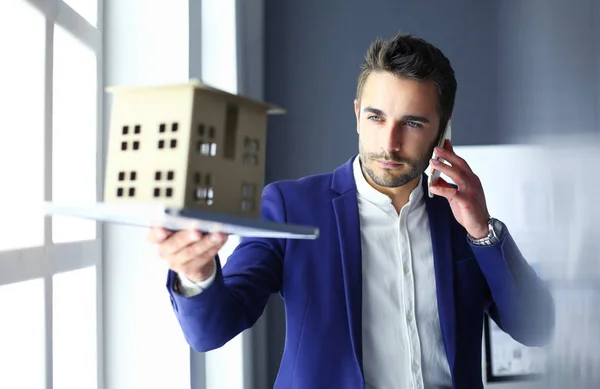 Homme d'affaires tenant maison miniature à portée de main debout dans le bureau . — Photo