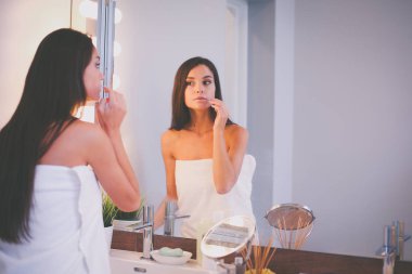 Çekici genç bir kadın yüzüne krem sürüyor.