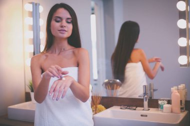 Çekici genç bir kadın yüzüne krem sürüyor.