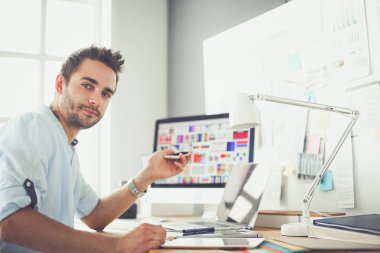 İnternette çalışırken bilgisayarın ve dizüstü bilgisayarın önünde grafik stüdyosunda oturan genç tasarımcının portresi.